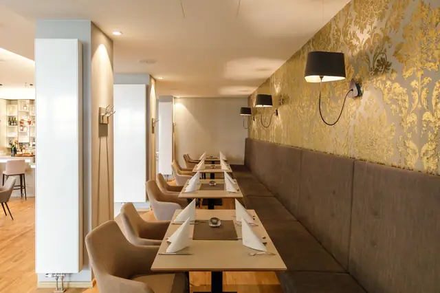 Lange gepolsterte Sitzbank im Luisenhof Dresden mit goldener Wandgestaltung, Tischen und Wandbeleuchtung